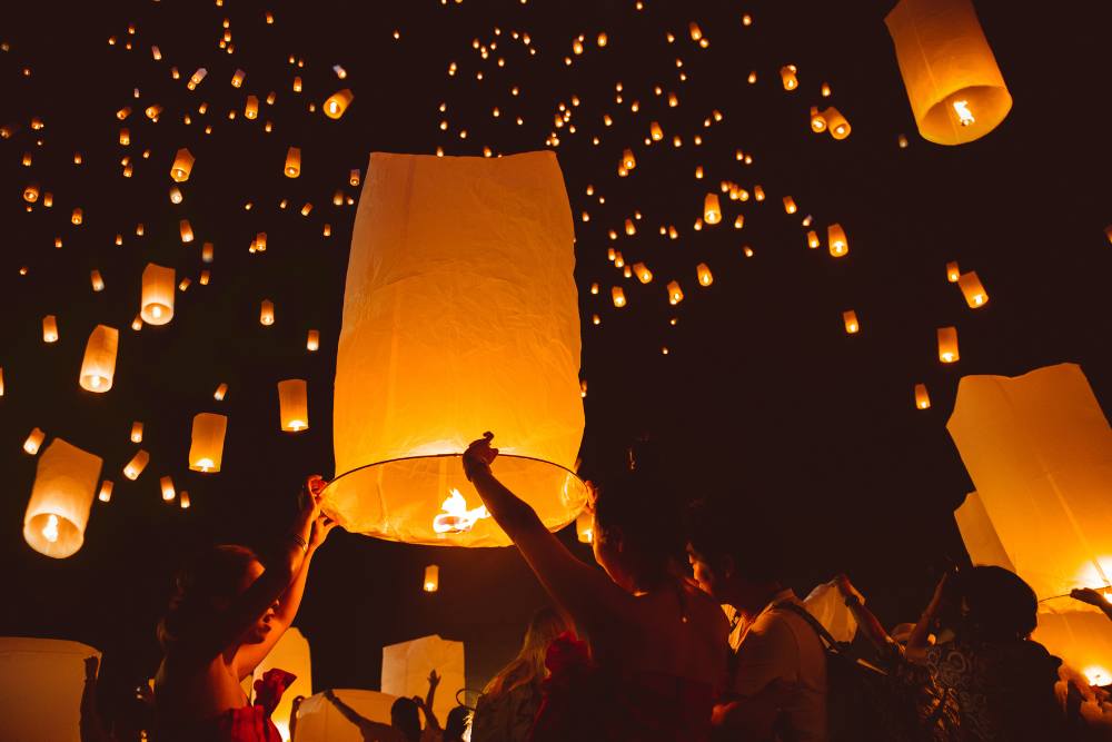 mains levant des lanternes célestes vers le ciel nocturne lors du festival Yi Peng à Chiang Mai