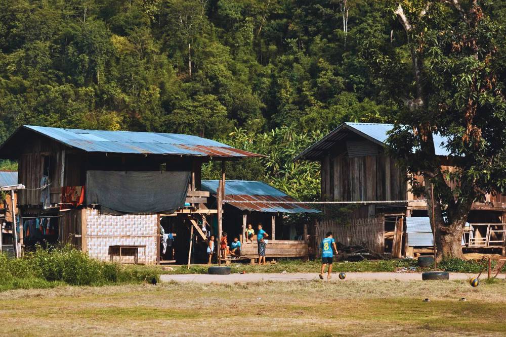 des garçons jouant au foot devant des maisons en bois dans le village de Huay Pu Keng