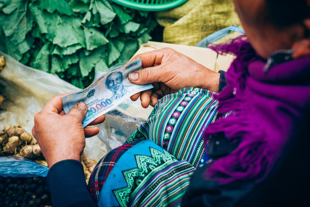 zoom sur vendeuse dans un marché ethnique tenant un billet de 20000 dong vietnam