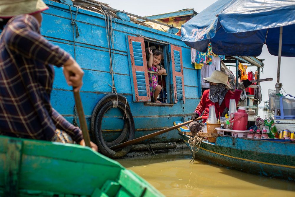 enfant dans un bateau faisant signe de la main, village flottant, lac Tonle Sap, Cambodge
