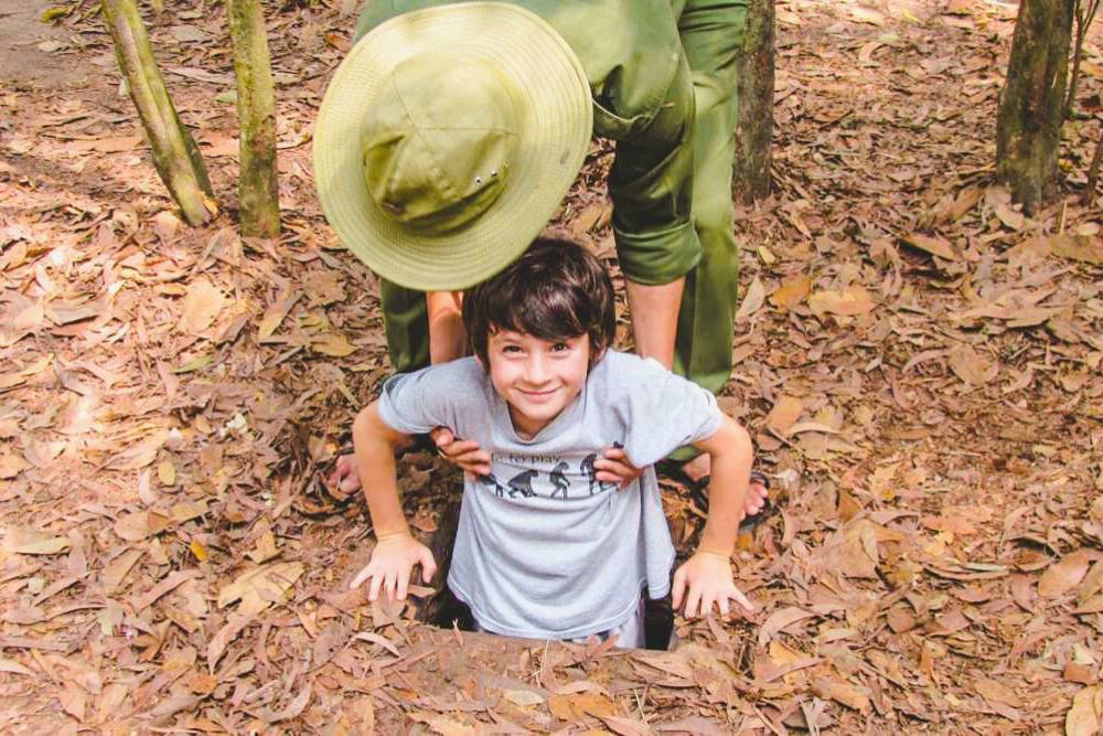 un enfant entre dans les tunnels de Cu Chi à l'aide d'un guide